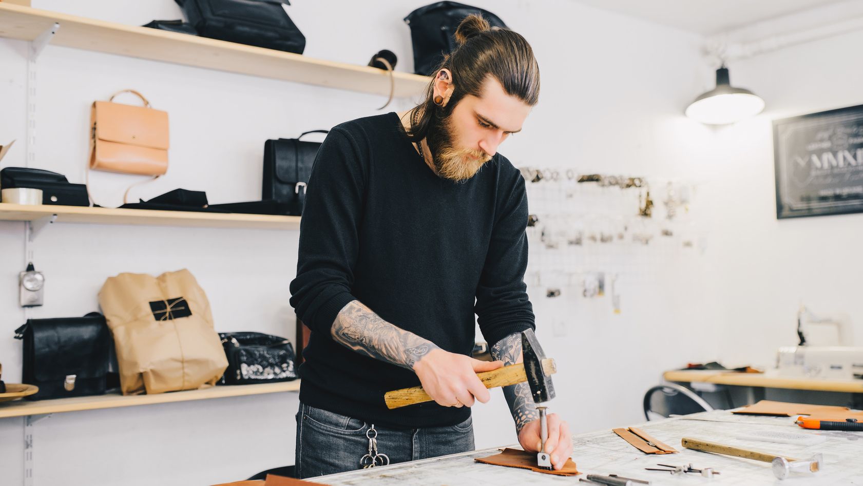 Leather craftsman working with leather using hammer. Working process in the leather workshop. Man holding crafting tool and working.