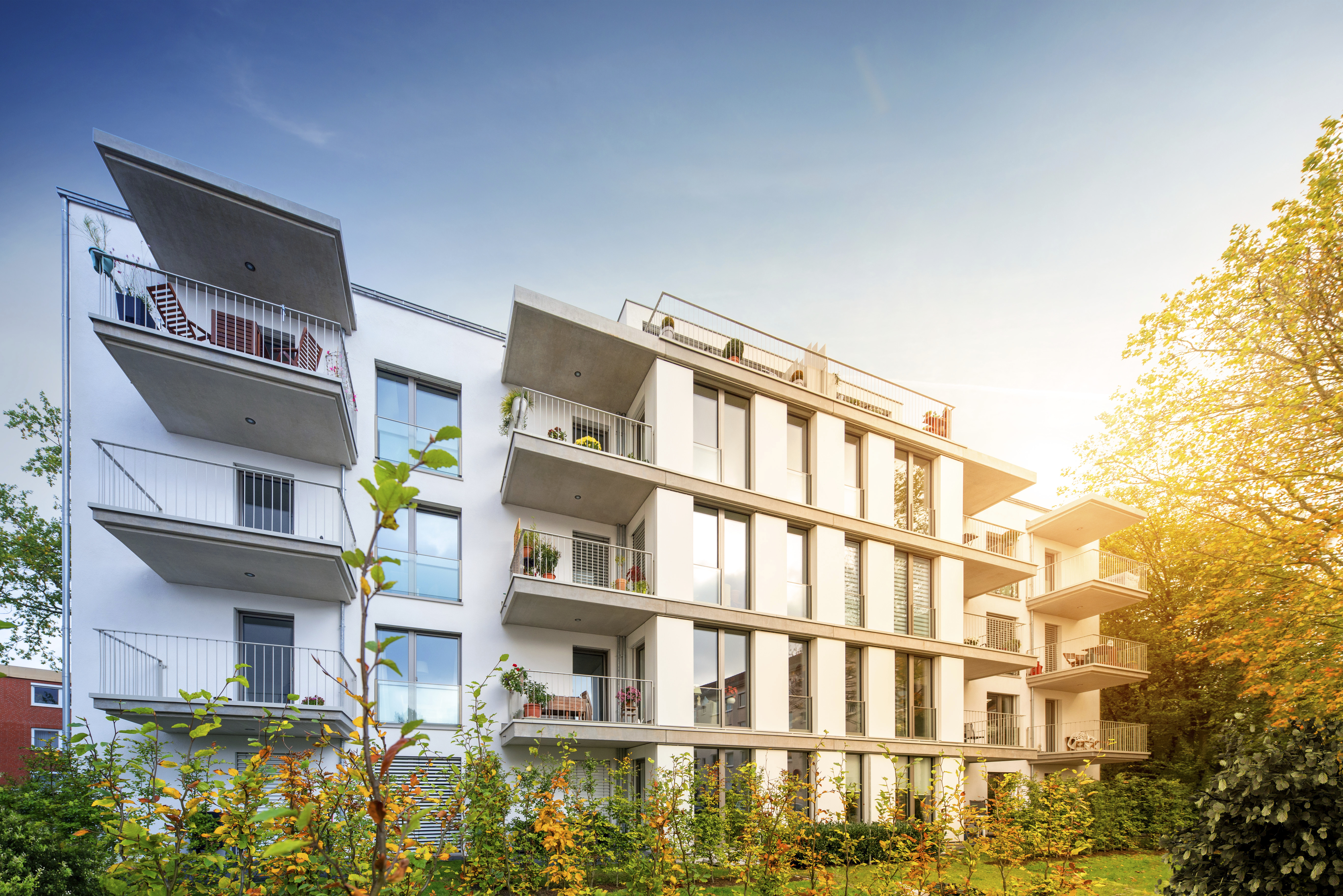 Weißes, mehrstöckiges Wohnhaus mit Balkonen im Grünen